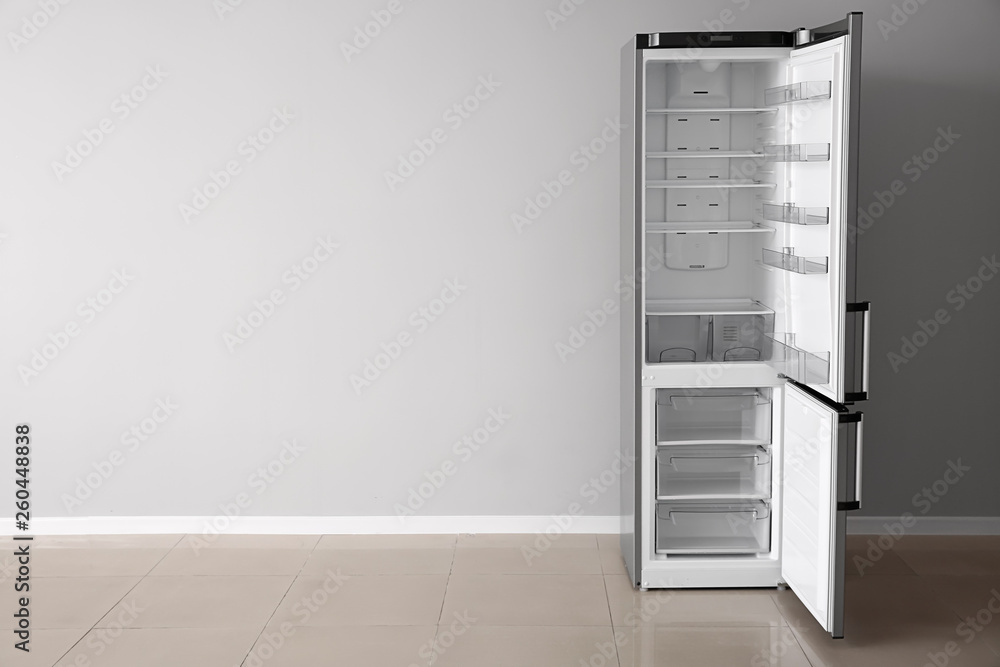 Open empty fridge near light wall