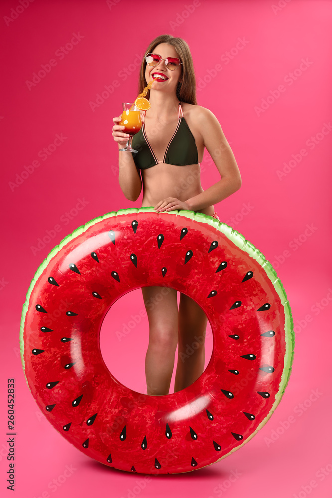 Beautiful young woman with inflatable ring and cocktail on color background