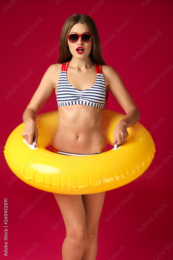 Surprised young woman with inflatable ring on color background