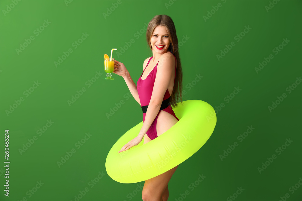 Beautiful young woman with inflatable ring and cocktail on color background