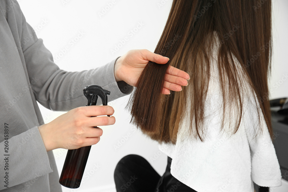 Hairdresser working with long hair of young woman in salon