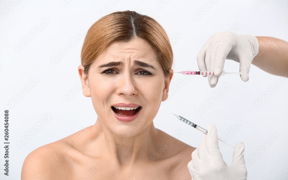 Scared woman and hands holding syringes for anti-aging injections on white background