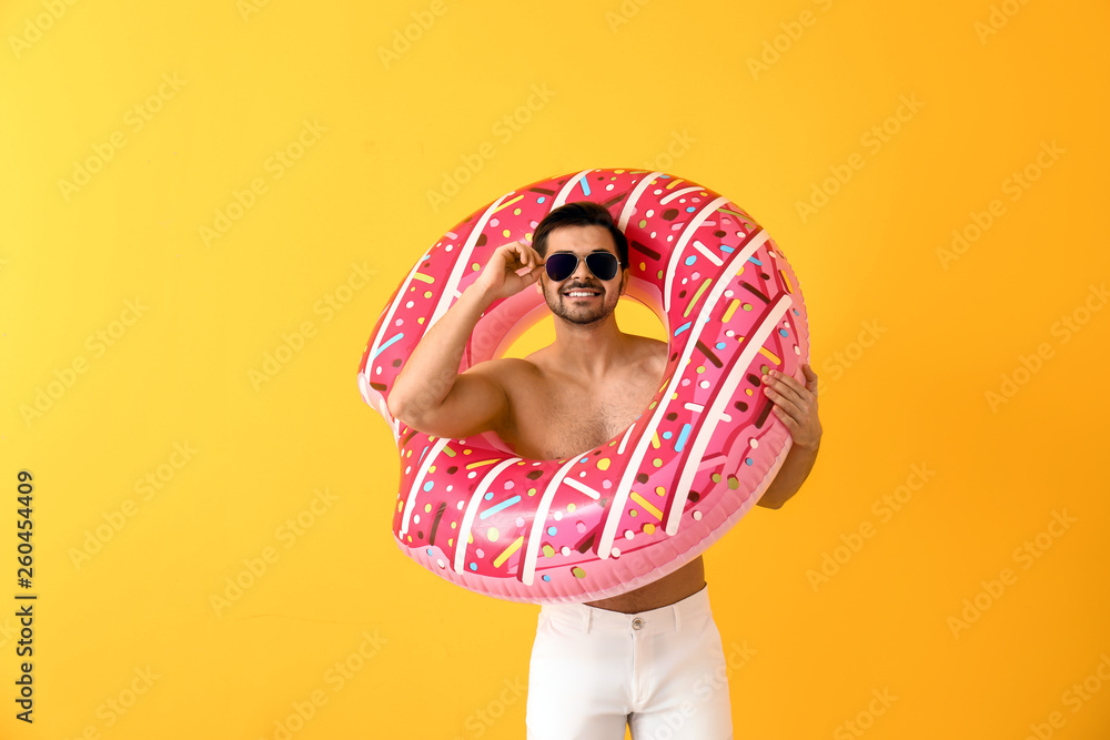 Handsome man with inflatable ring on color background