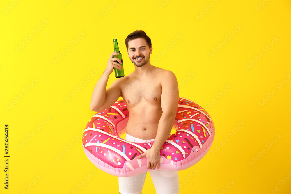 Handsome man with inflatable ring and beer on color background