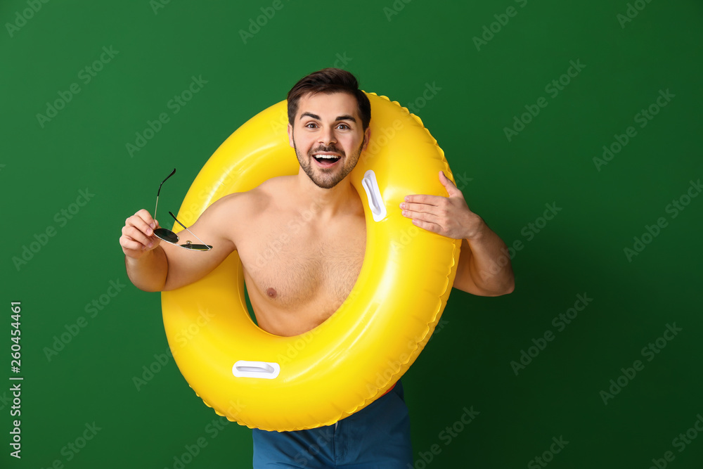 Handsome man with inflatable ring on color background