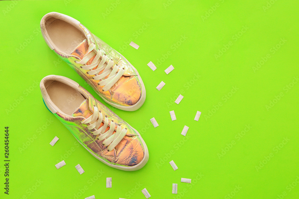 Stylish shoes from iridescent material on color background