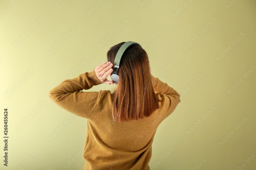 Young woman with headphones listening to music on color background