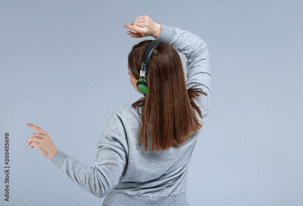 Young woman with headphones listening to music on grey background