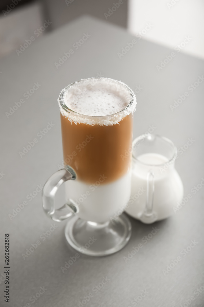 Glass cup of tasty frappe coffee and jug of milk on grey table