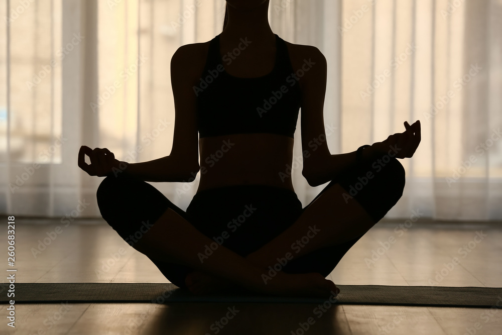 Silhouette of woman practicing yoga indoors