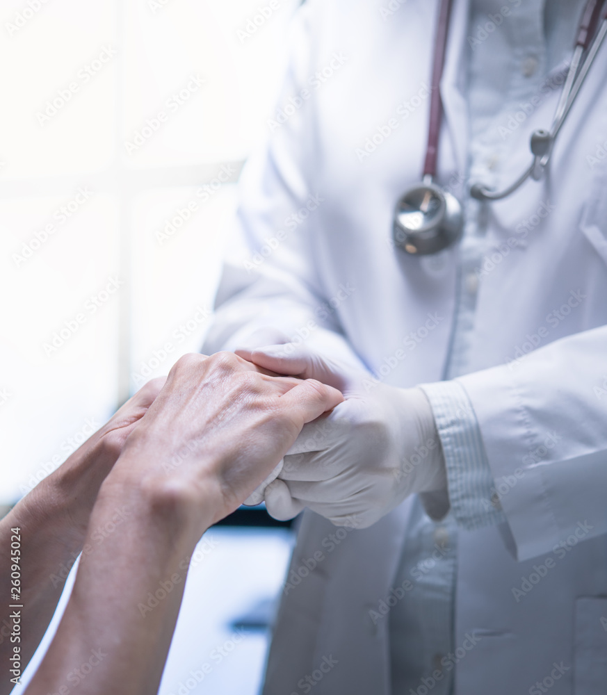 Medical doctor wearing latex gloves holding patient’s hand to give support in hospital setting