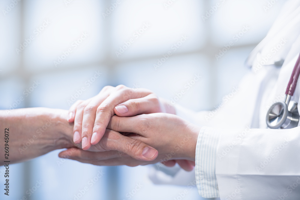 Medical doctor reassuring patient by holding patient鈥檚 hands in hospital setting