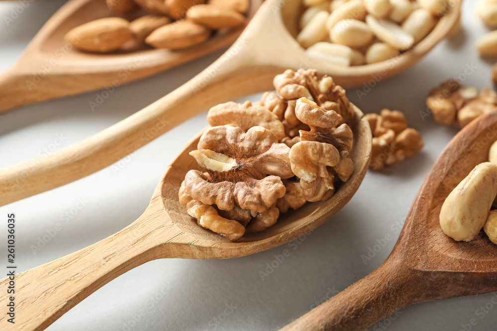 Wooden spoon with tasty walnuts on light background