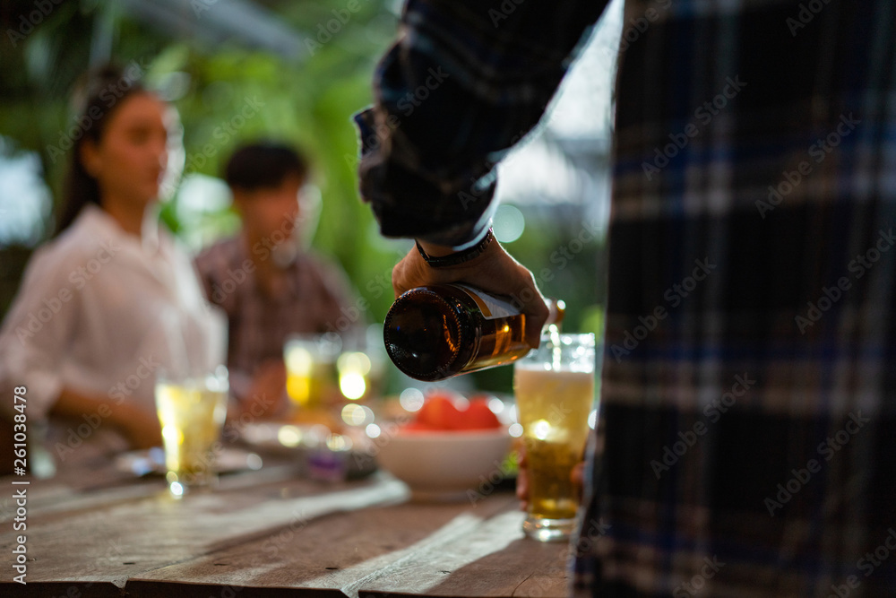 Asian group eating and drinking cold beer outside the house at night, having fun talking