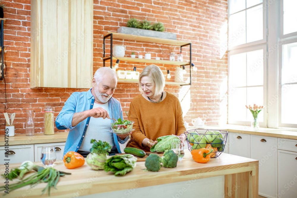 Cheerful senior couple eating salad standing together with healthy food on the kitchen at home. Conc