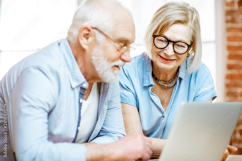 Portrait of a beautiful senior couple in blue shirts feeling happy, sitting together with laptop at 