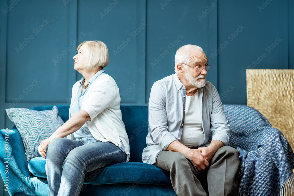 Offended senior man and woman feeling sad, sitting back to each other on the couch at home