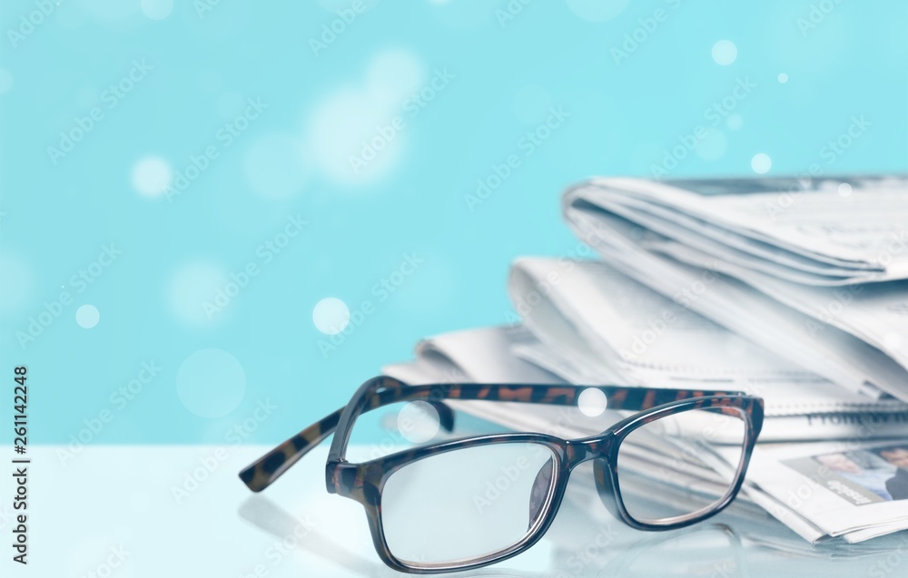 Newspapers with reading glasses on background