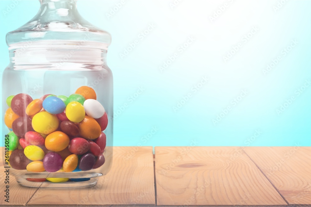 Transparent glass jar with colorful chocolate candies on table