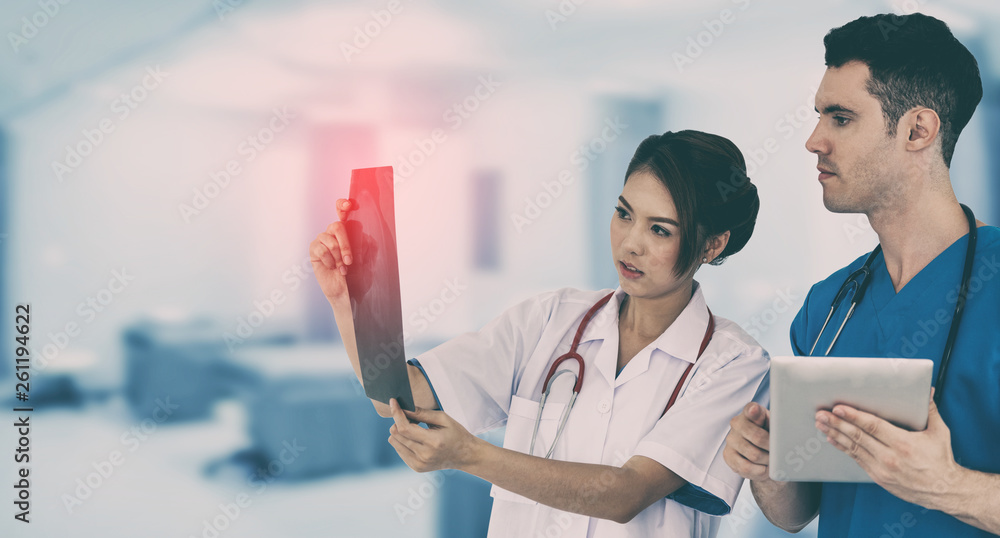 Female doctor looking at x ray film while discussing with another doctor holding a tablet computer a