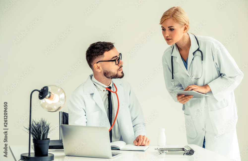 Doctor at hospital office working on laptop computer on the table with another doctor having discuss