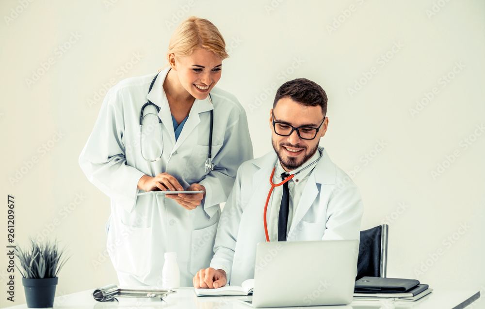 Doctor at hospital office working on laptop computer on the table with another doctor having discuss