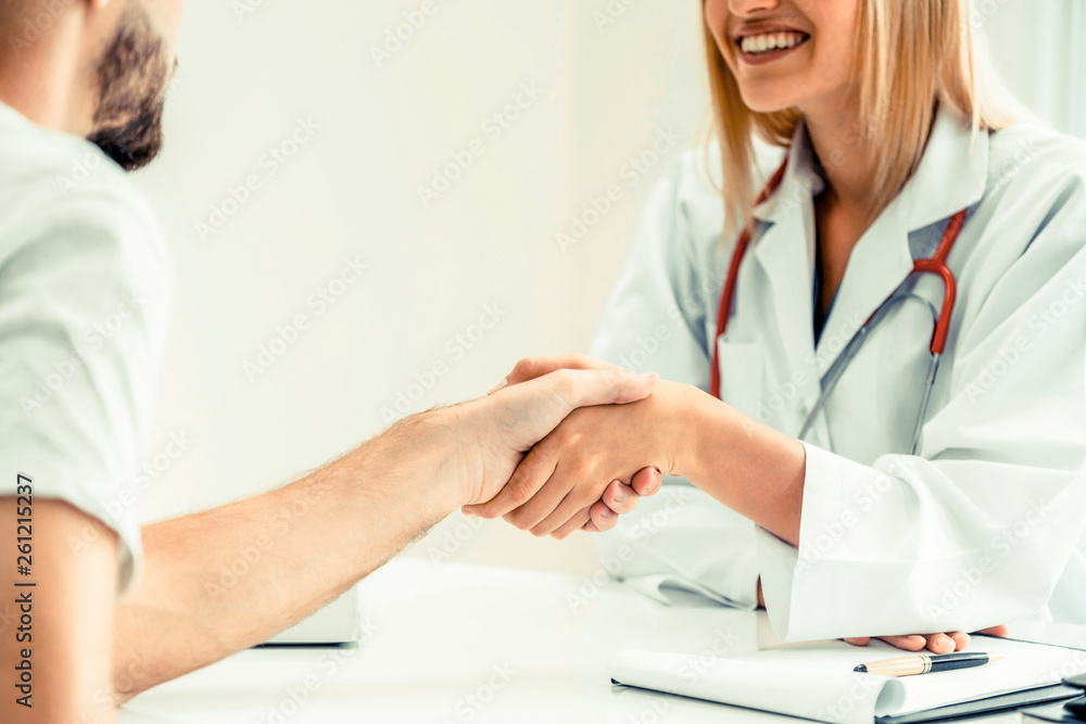 Woman doctor doing handshake with male patient in hospital office room. Healthcare and medical servi