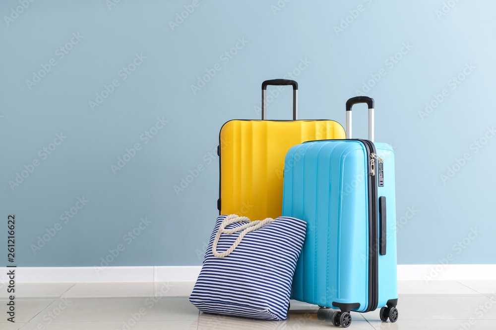 Packed suitcases and beach bag near color wall