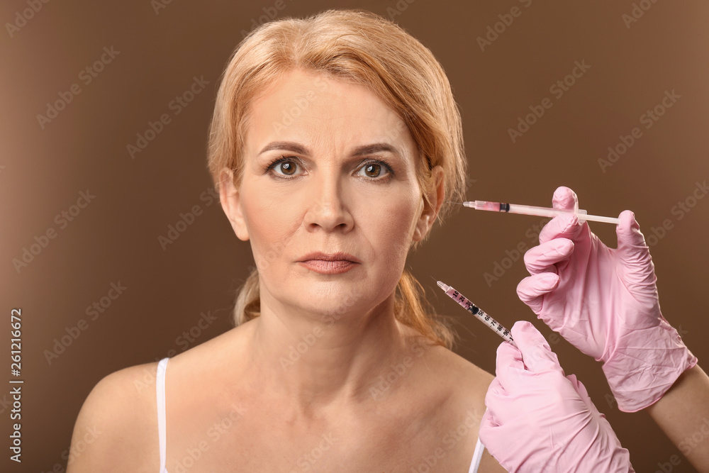 Mature woman and hands holding syringes for anti-aging injections on color background