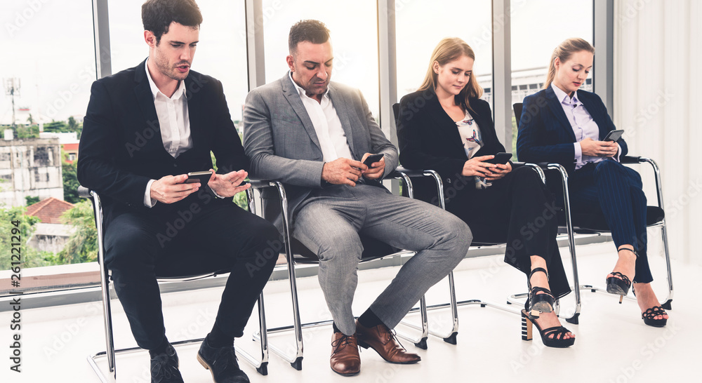 Businesswomen and businessmen using mobile phone while waiting on chairs in office for job interview