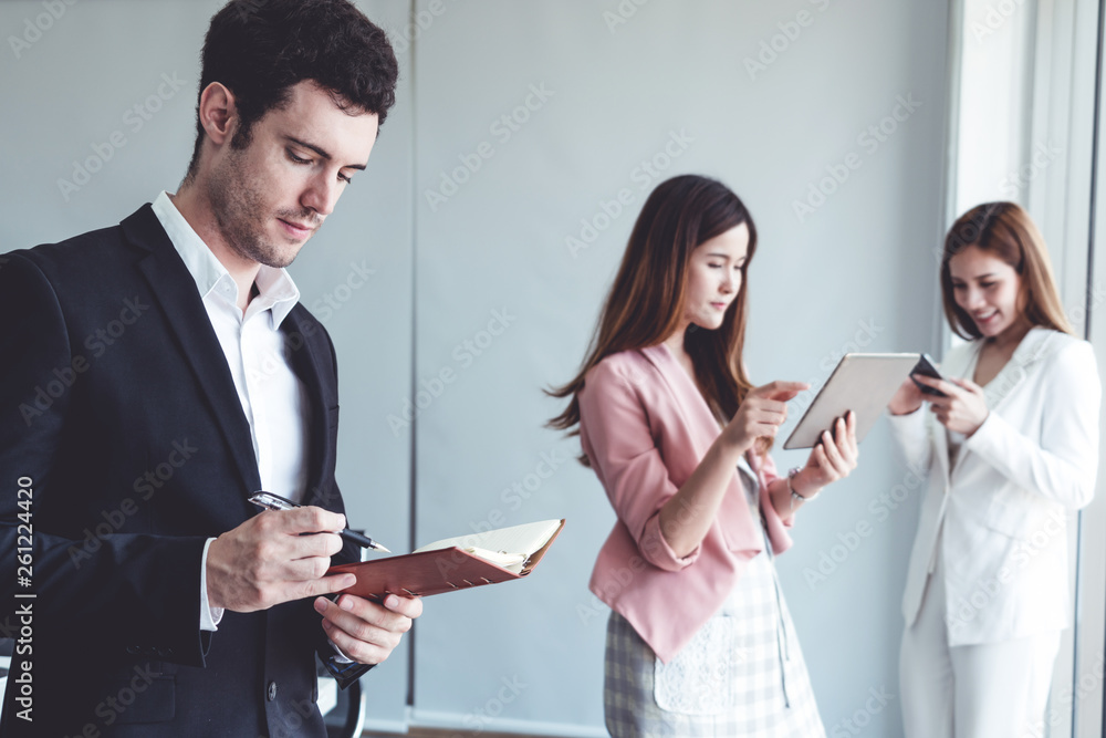 Happy young handsome businessman reading book and working in office with colleagues and friend at wo