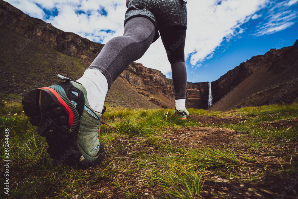 Woman traveler trekking in Icelandic summer landscape at the Hengifoss waterfall in Iceland. The wat