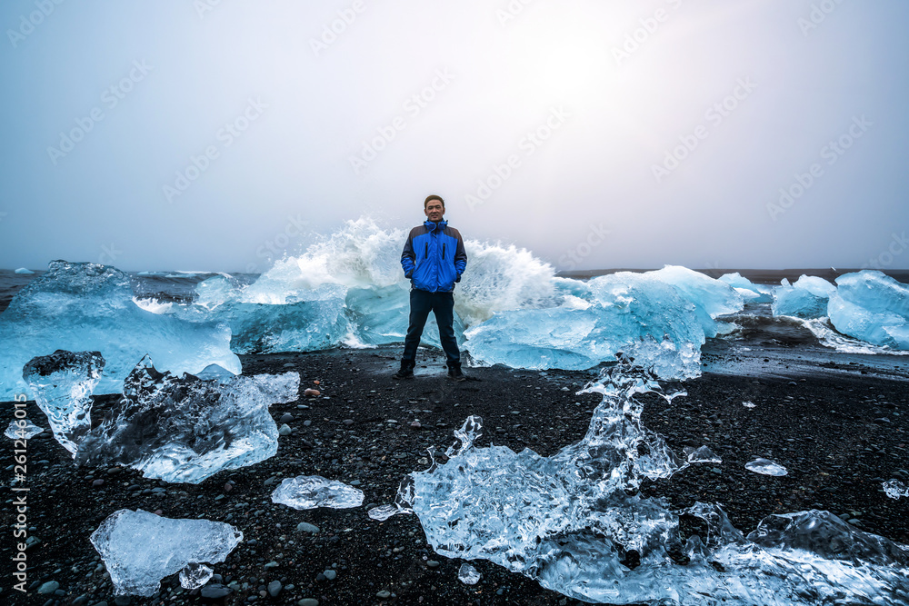 Young man traveler travel to Diamond Beach in Iceland. Frozen ice on black sand beach known flows fr