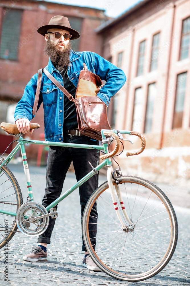 Lifestyle portrait of a bearded hipster dressed stylishly with hat and jacket standing with retro bi