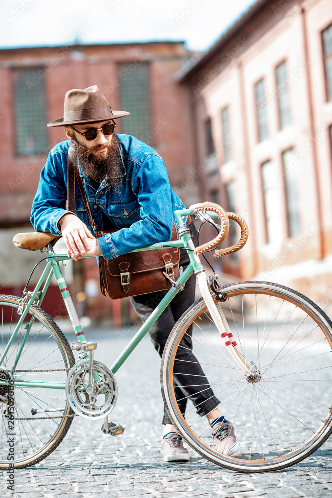 Lifestyle portrait of a bearded hipster dressed stylishly with hat and jacket standing with retro bi