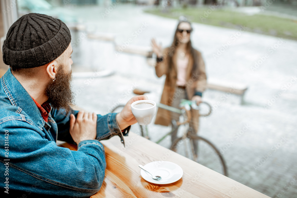 Stylish man meeting his girlfriend with bicycle while sitting with coffee near the window at the caf