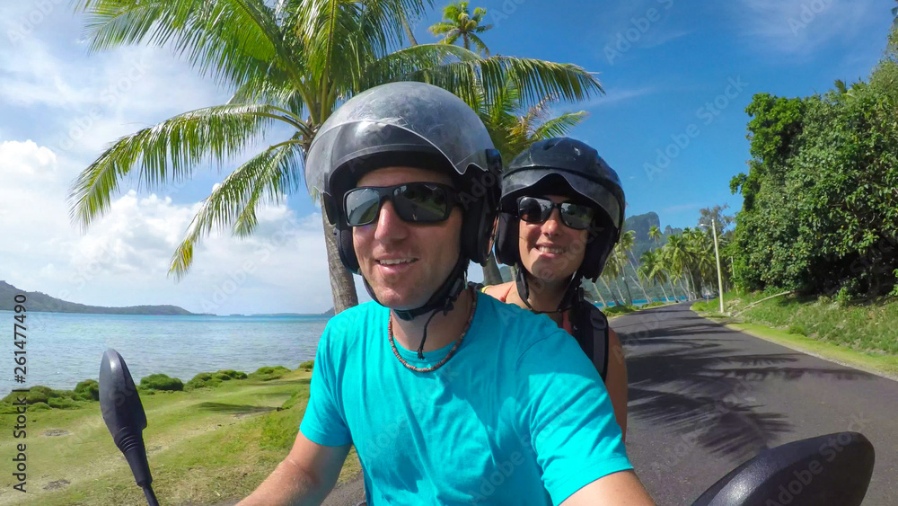 SELFIE: Cheerful man and woman riding on a scooter along the scenic coastal road