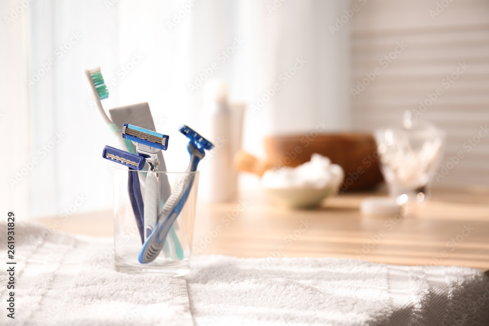 Glass with razors, tooth paste and brush on table in bathroom