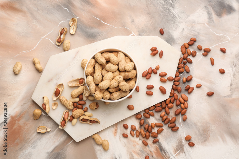 Bowl with tasty peanuts on color background