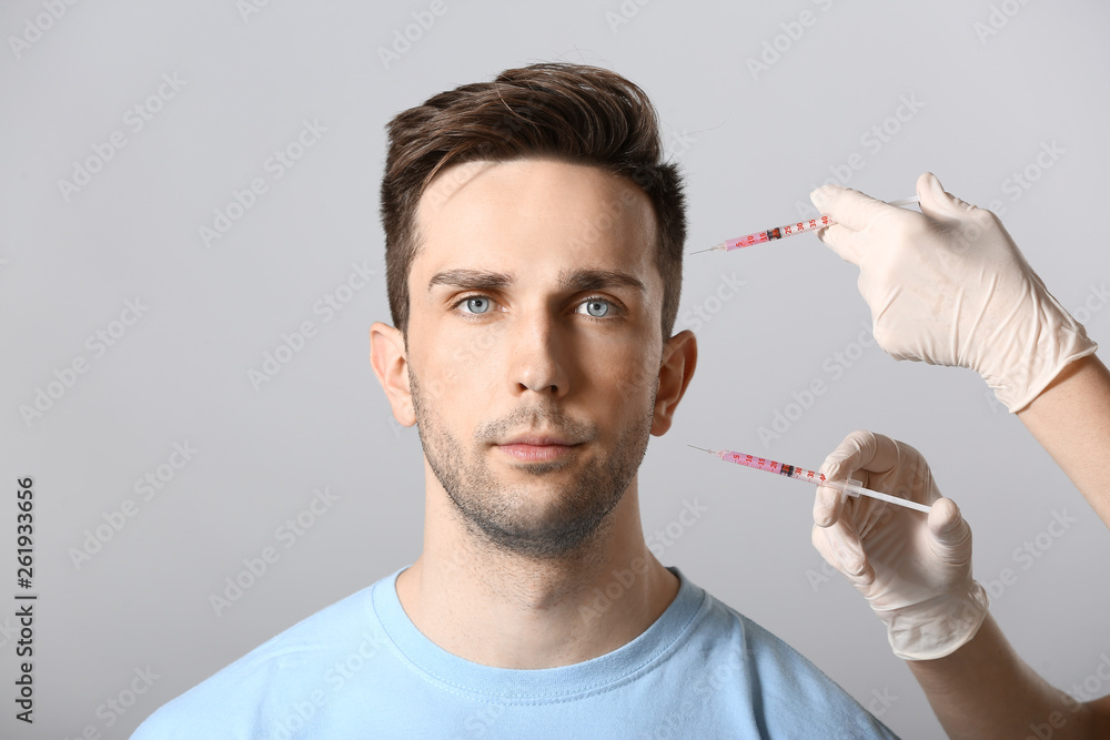 Handsome man and hands holding syringes for anti-aging injections on light background