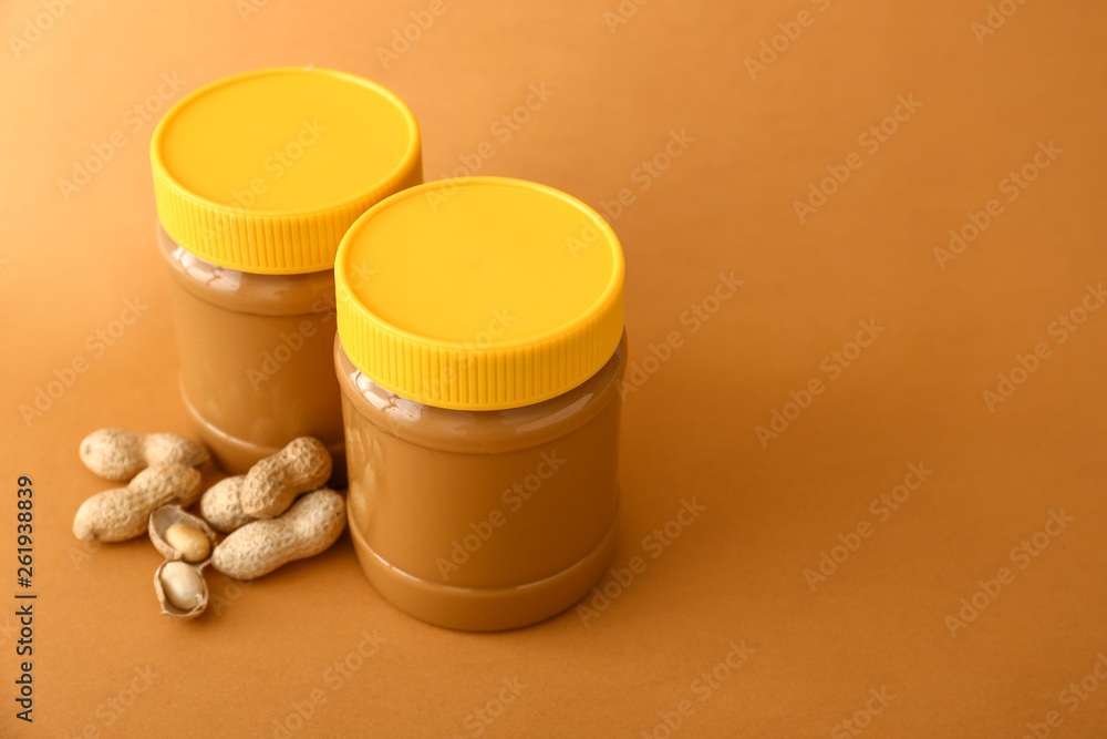 Tasty peanut butter in jars on color background