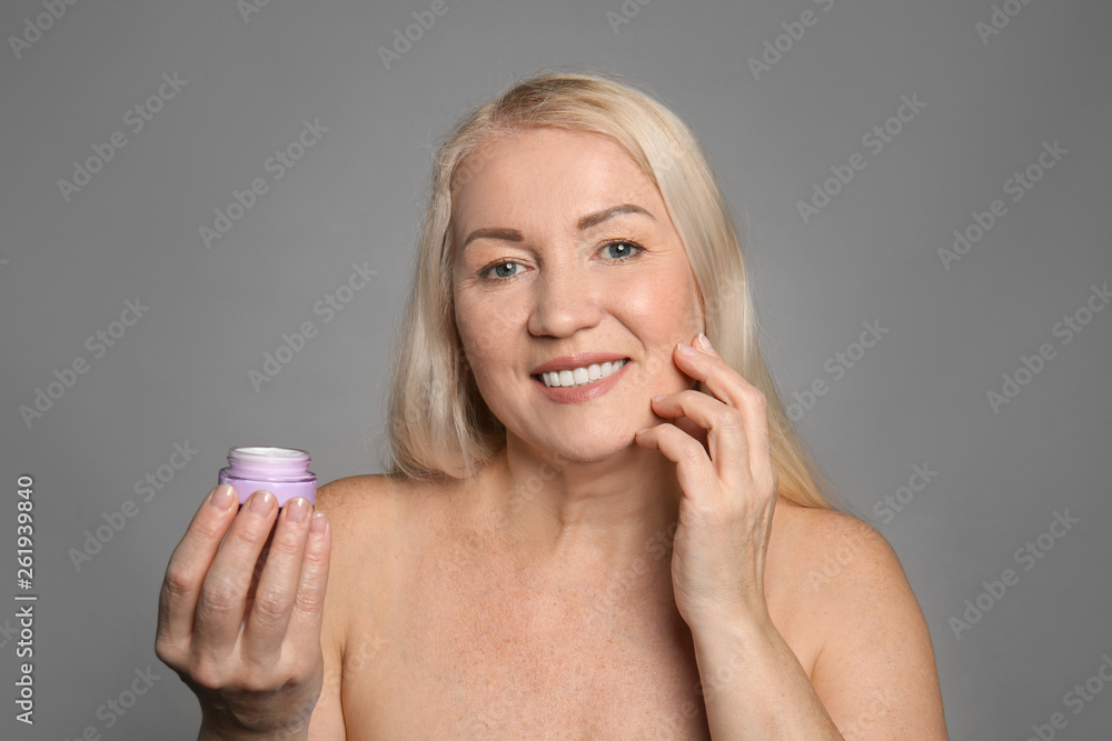 Mature woman with jar of cream on grey background