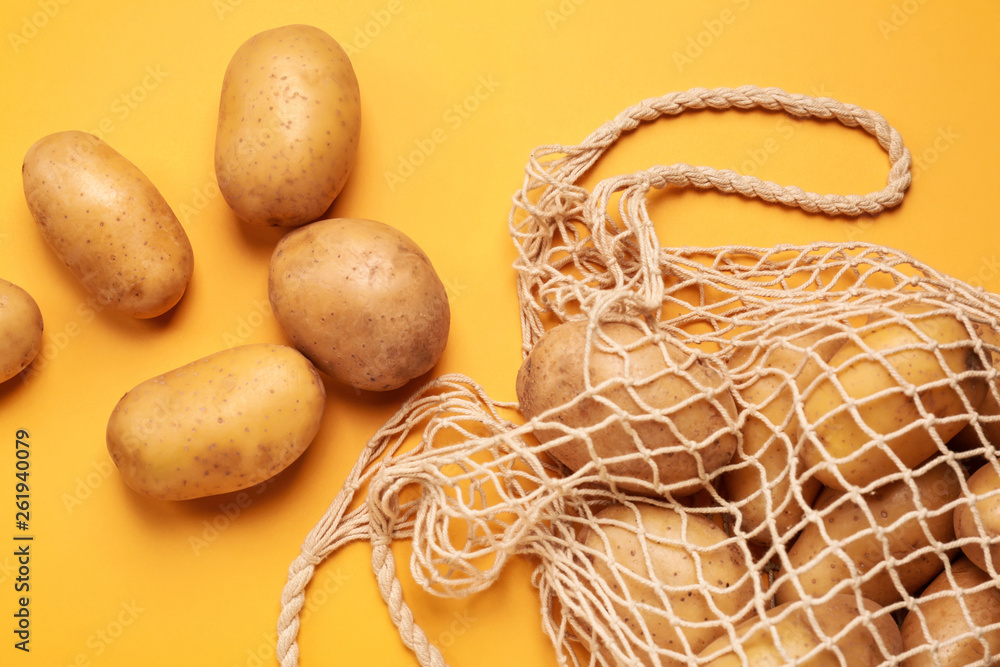 String bag with raw potatoes on color background