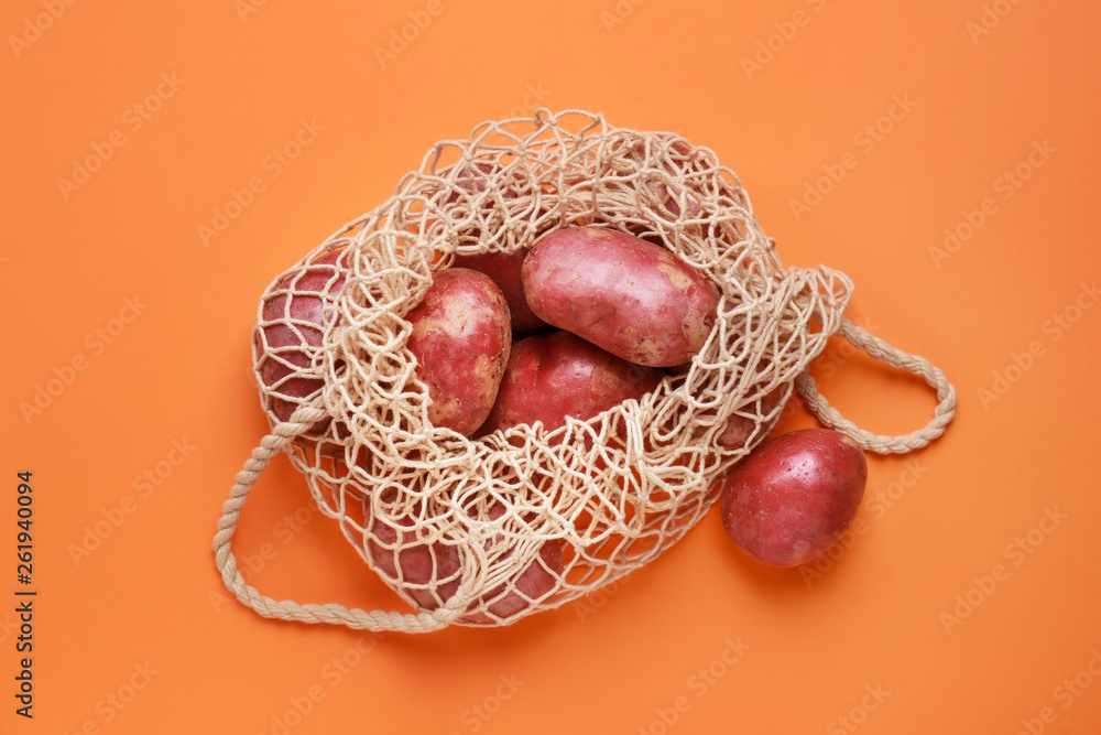 String bag with raw potatoes on color background