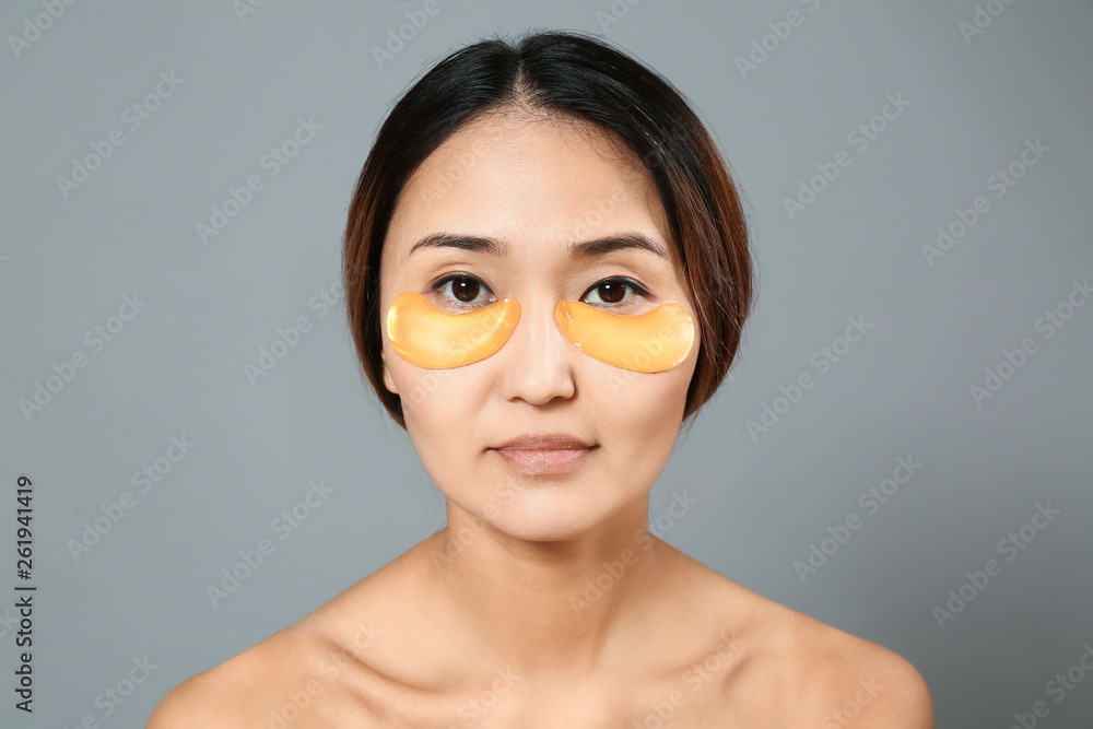 Asian woman with under-eye patches on grey background