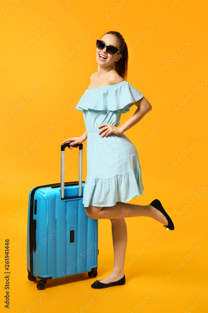 Female traveler with suitcase on color background