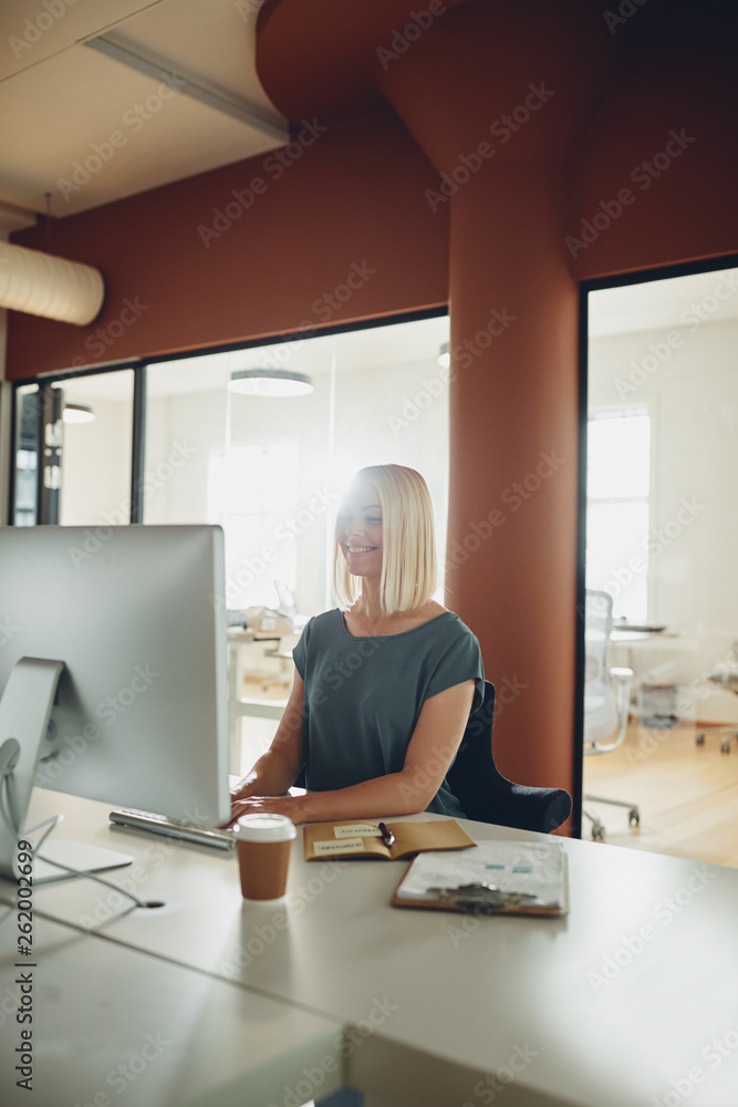 Smiling young businesswoman working online at her office desk