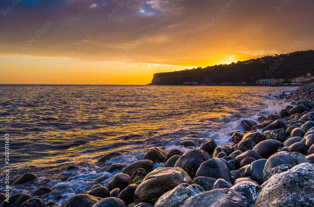 Panorama view of amazing ocean scenery with rocks on a beach in beautiful golden evening light at su