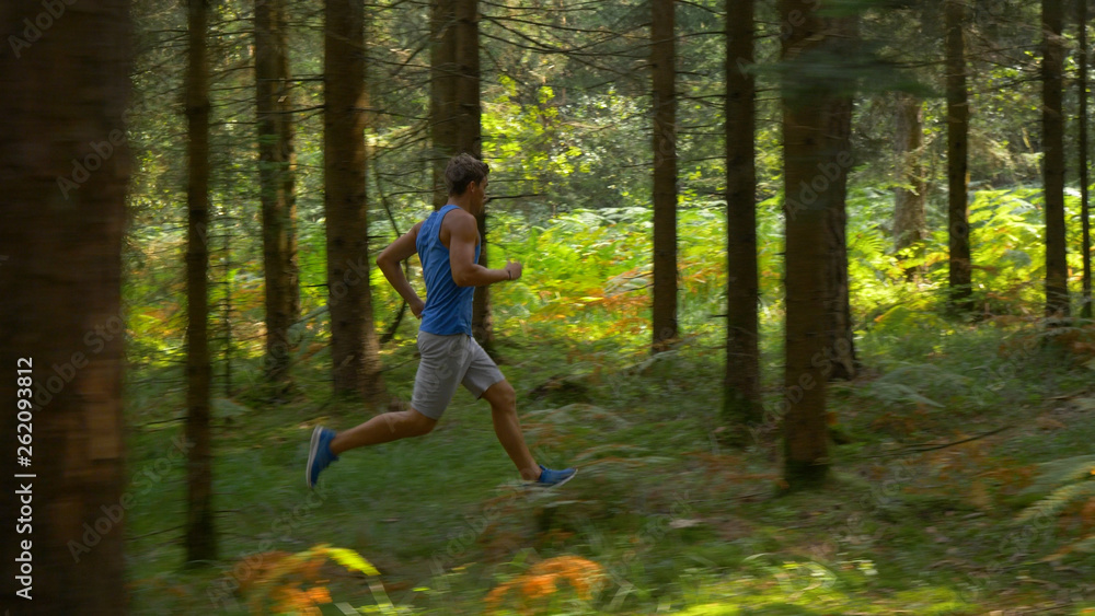 Male athlete sprinting during a trail running race through the tranquil forest.