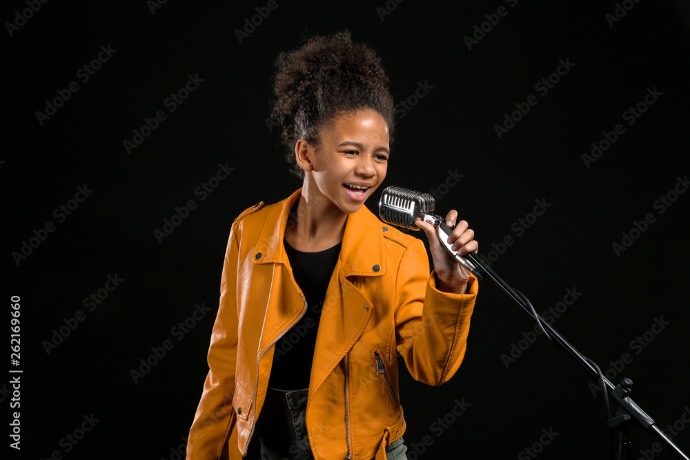 African-American girl with microphone singing against dark background